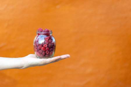 Close up cropped photo of transparent crystalline container with raspberries on worker lady hands...