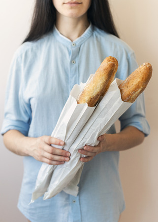 Cropped vertical photo of young confident sucsess feminine woman in blue formalwear uniform shirt isolated on pastel background made bread, hold it in hands focus on gold crust baguettesの写真素材