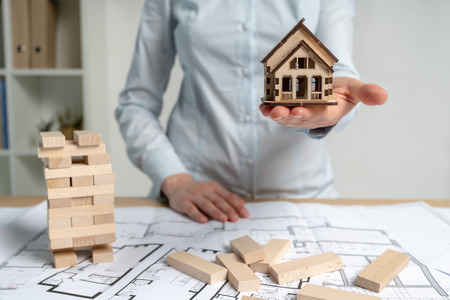 Consumer and consumerism concept. Businesswoman in her formal wear standing indoor light workplace office. She holding little house object in hand making opportunity for rental flat or apartmentの写真素材