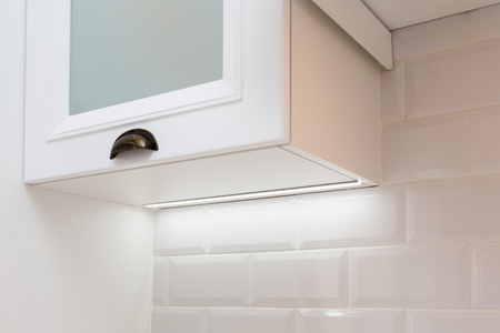 Close up and low angle top view photo of luxury interior element. Door handle on small white kitchen shelf with lightの写真素材