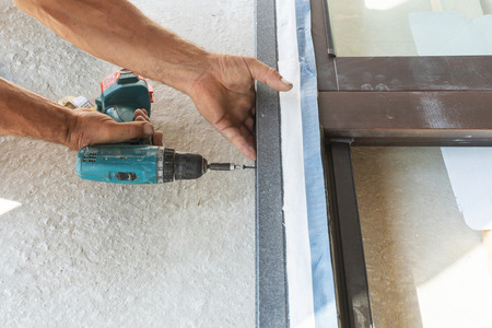 Close up cropped photo of adult handyman using torque screwdriver and assembly new plastic window frameの写真素材