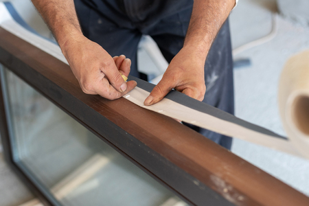 Close up photo of adult handyman glue special protective tape on wooden window frameの写真素材
