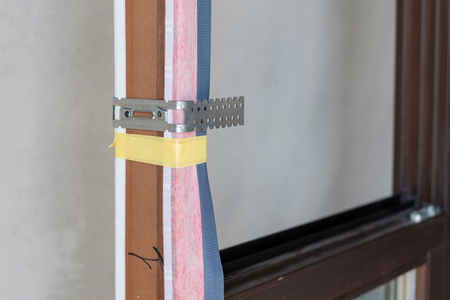 Close up detail of metal anchor plate above protective glue tape on wooden window frameの写真素材