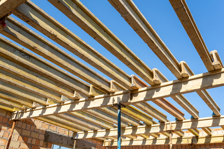 Low angle top view photo of formwork construction. Small unfinished building with wooden ceiling beam on support pipes under blue skyの写真素材