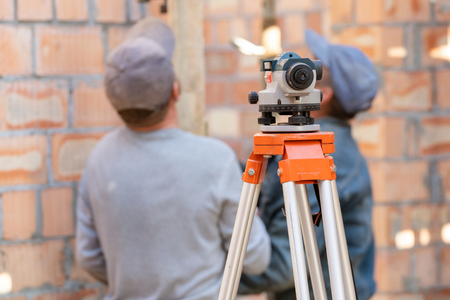 Formwork construction concept. Selective focus on optical level device against unrecognizable and blurred professional workmanの写真素材
