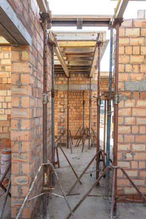 Formwork construction concept. Vertical photo of unfinished building with wooden beam under roof and metal support pipesの写真素材