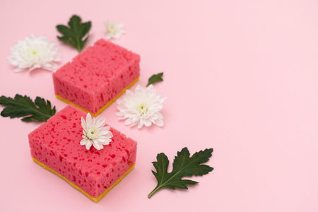 Two polyurethane sponges with white flowers and green leaves laying isolated on pastel pink...