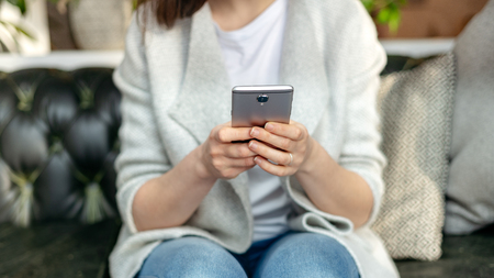 Cropped and close up photo of lady in trendy wear sitting inside loft interior space in restaurant. She holding portable telephone equipment in her handsの写真素材
