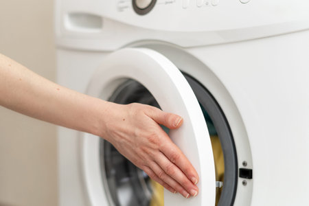 Close up and cropped photo of laundry process. Woman holding her hand on closed door of washing...