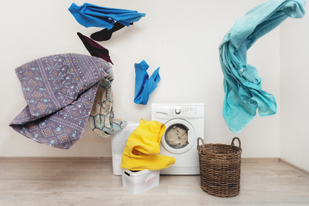 Concept of funky and easy laundry process. White washing machine standing inside flat with bright interior near flying multicolored clothesの写真素材