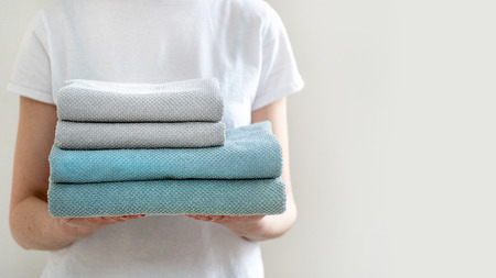 Concept of finished laundry. Cropped photo of nice and peaceful lady with towels in hands standing inside bright light flat interiorの写真素材