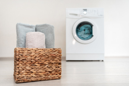 Laundry basket with clean and rolling towel standing inside bright light flat interior against blurred washing machineの写真素材