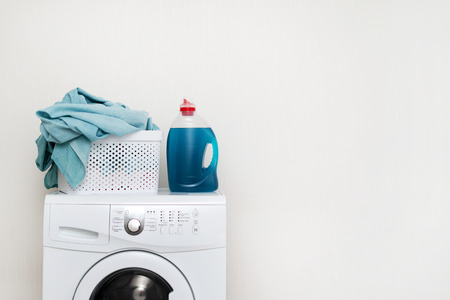 Concept of laundry process. White washing machine standing isolated inside bright light flat interior. Gel detergent soap with basket of lien on top of laundromatの写真素材