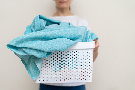 Close up photo of beautiful woman with basket of linen in hands. Laundry process inside bright apartment interiorの写真素材