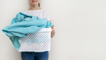 Cropped photo of positive and cheerful lady with plastic laundry basket in hands. She standing against wall inside flat with bright interior and making nice smileの写真素材
