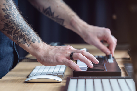 Profile side view and close-up cropped photo tattoo hands of creativity disc jockey. Man playing on mini piano keyboard and creative music in black modern and sound studio with style interiorの写真素材
