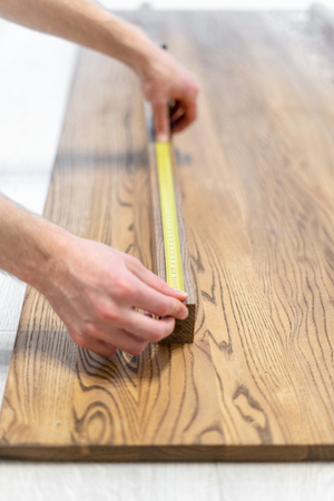 Vertical and selective photo of carpenter person with special yellow measuring type equipment in hand and checking size of new wooden desk or table topの写真素材