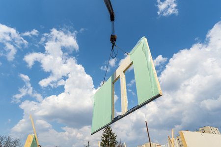 Process of construction new and modern modular house from composite sip panels. Low view angle photo of crane with sip panel against sky and blue backgroundの写真素材