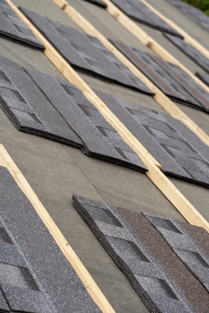 Vertical photo of layer of installing asphalt or bitumen shingle on top of the new roof under...