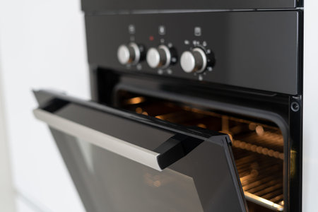 Selective focus of black and modern built in oven with open glass door on white contemporary kitchenの写真素材