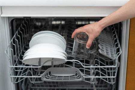 Cropped view of woman standing on kitchen near built in, opened and modern dishwasher machine with...