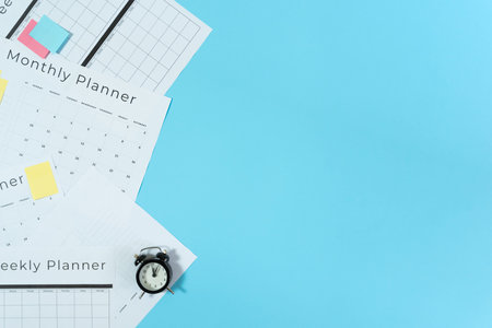 Top view of alarm clock, monthly and weekly planner with copy space and sticky notes on pastel blue...