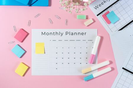 Top view of folders, monthly planner, colorful sticky notes,  stationery, marker and paperclip on pastel pink background with copy spaceの写真素材