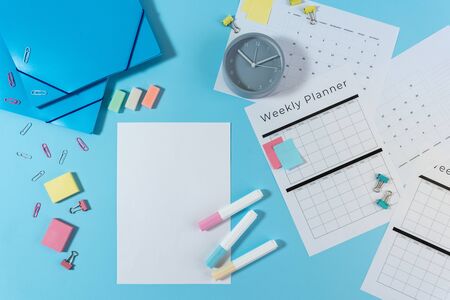 Top view of alarm clock, stationery, weekly planner and empty paper with copy space on pastel blue backgroundの写真素材