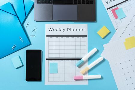 Top view of modern laptop, smartphone, colorful stationery and weekly planner with copy space on pastel blue backgroundの写真素材