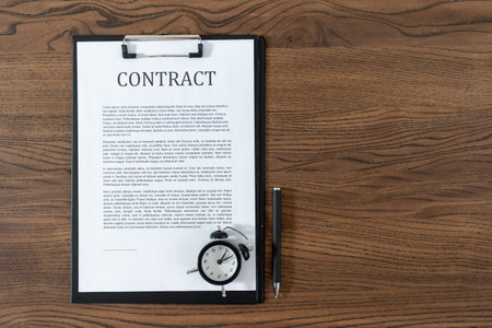 Top view of contract, alarm clock and stationery pen at wooden table with copy space