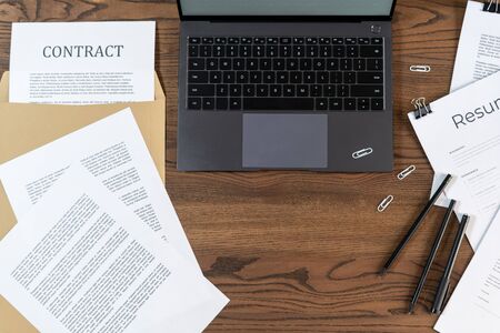 Top view of modern laptop and documents, contract, stationery on wooden table with copy space in officeの写真素材
