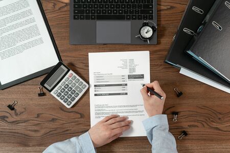 Top view of bookkeeping woman working with bills, counting savings and investment on calculator, sitting at office behind wooden tableの写真素材