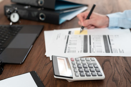 Selective focus of calculator near laptop computer, bills documents, stationery at wooden table and...