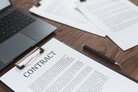 Contract in clipboard lying at office on wooden table with  laptop and documentsの写真素材