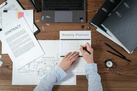Top view of engineer designer working with weekly planner, sitting in office with laptop computer, architecture plan, blueprint and documents on wooden tableの写真素材