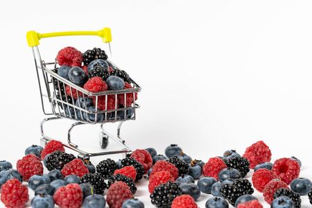 Close up view of shopping cart trolley with ripe blueberry, blackberry and raspberry on white background with copy spaceの写真素材