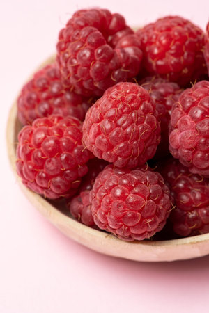 Vertical photo and close up view of sweet, red and ripe raspberry fruits in wooden bowl on pastel...