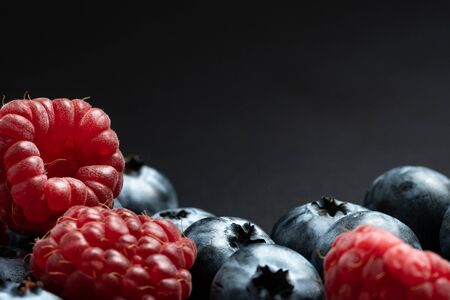 Selective focus and close up view of mix different ripe and sweet blueberries, raspberries fruits on black background with copy spaceの写真素材