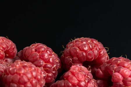 Macro view of red and ripe raspberries fruit on black background with copy space