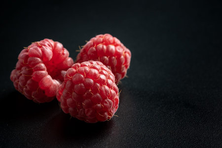 Close up view of red and ripe raspberries fruit on black background with copy space