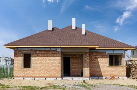 Photo of real and new modern brick house under construction with white chimney and roof shingles installed on topの写真素材