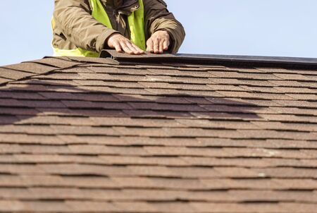 Building under construction concept. Workman installing roof asphalt shingles or tiles installed on top of the new residential houseの写真素材