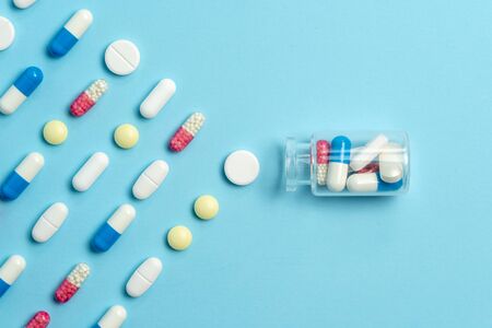 Painkillers and healthcare concept. Top view and flat lay of set with different pills and tablets lying in line near gladd bottle on blue background with copy spaceの写真素材