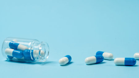 Selective focus of glass bottle with medical pills capsules on blue background with copy space