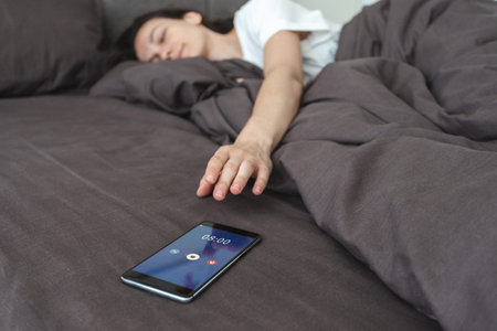 Selective focus of calm young adult woman snooze in bed and switch off alarm clock notification on...