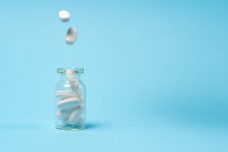 Treatment and healthcare concept. White medical pills drops in glass bottle with medicaments on blue...