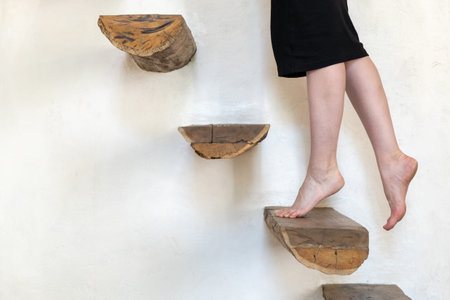 Cropped view of young adult woman in dress standing on wooden stairs against white wall at home....