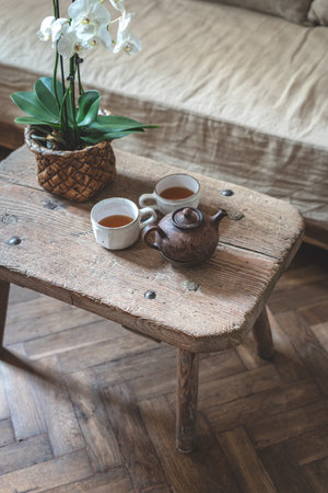 High angle view of teapot, mugs with tea and white orchid flower in flowerpot on table. Vertical...