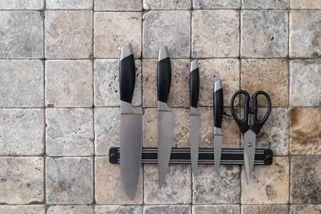 Textured marble stone and square tile on wall  with set of cooking knives and scissors. Element of kitchen interior in cozy house with copy spaceの写真素材
