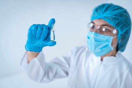 Healthcare development concept. Selective focus of laborant woman in lab uniform holding ampoule with vaccine in hands, standing isolated on white backgroundの写真素材
